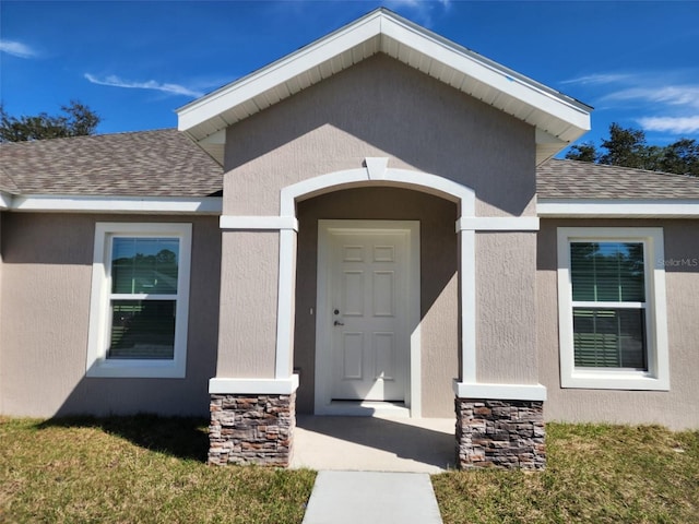 doorway to property featuring stucco siding, stone siding, and a shingled roof