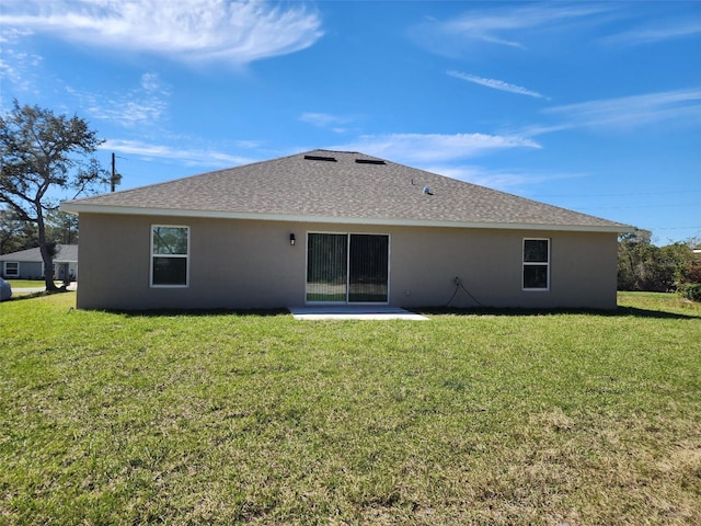 rear view of property with stucco siding, a lawn, and roof with shingles