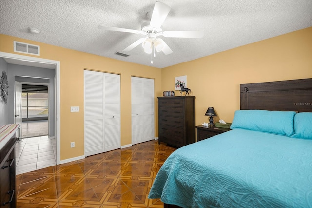 bedroom with a textured ceiling, two closets, and visible vents