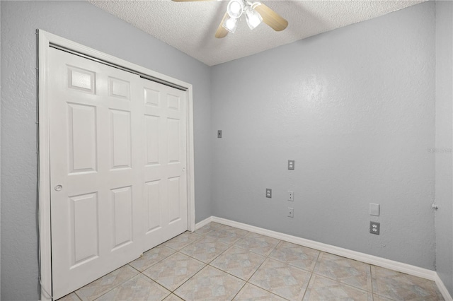 unfurnished bedroom with light tile patterned floors, a closet, a ceiling fan, a textured ceiling, and baseboards