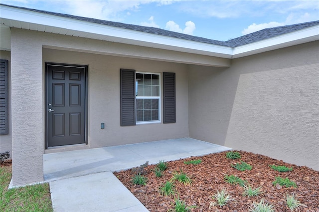 doorway to property with roof with shingles and stucco siding