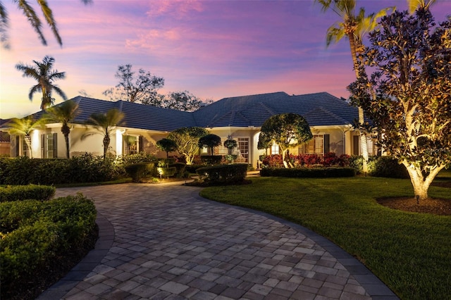 view of front facade featuring stucco siding, decorative driveway, and a yard