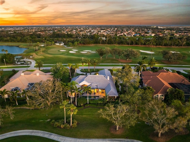 aerial view at dusk featuring view of golf course and a water view