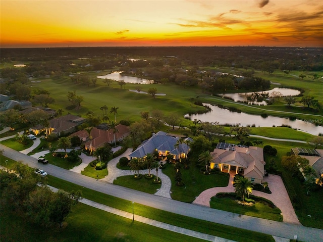 aerial view at dusk featuring view of golf course and a water view