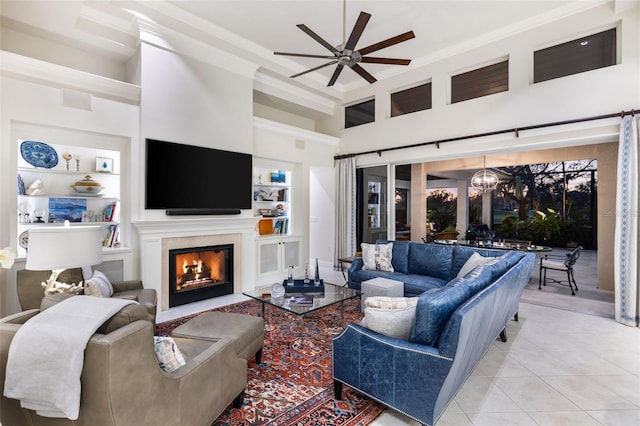 living room with light tile patterned floors, built in features, a fireplace with flush hearth, a high ceiling, and ceiling fan with notable chandelier