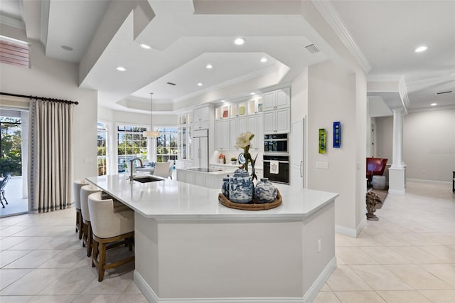 kitchen featuring plenty of natural light, decorative columns, a large island, a tray ceiling, and a sink