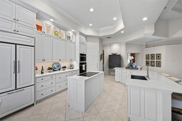 kitchen featuring paneled fridge, black electric stovetop, a spacious island, a sink, and crown molding