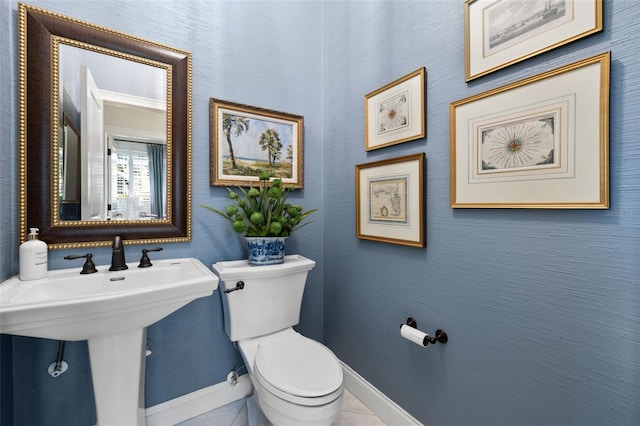 half bath with baseboards, a sink, toilet, and tile patterned floors