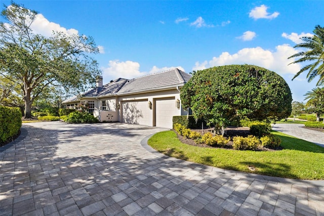 view of front of home featuring a garage, decorative driveway, a chimney, and stucco siding