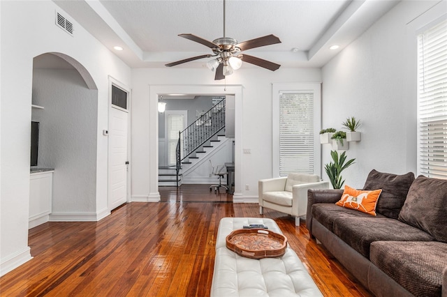 living room with stairway, visible vents, a tray ceiling, and hardwood / wood-style floors