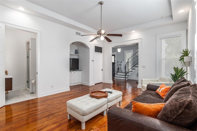 living area with arched walkways, stairway, wood finished floors, and baseboards