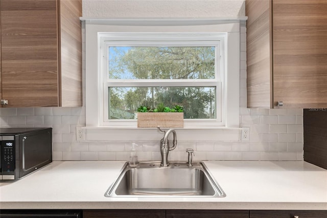 kitchen featuring black microwave, light countertops, plenty of natural light, and a sink
