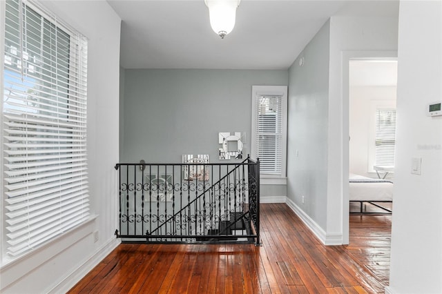 hall featuring baseboards, hardwood / wood-style floors, and an upstairs landing