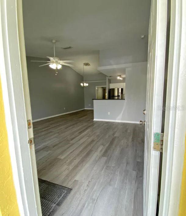 unfurnished living room featuring wood finished floors, baseboards, visible vents, lofted ceiling, and ceiling fan