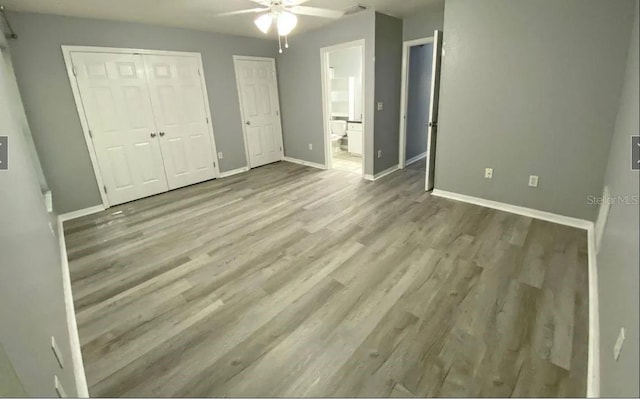 unfurnished bedroom featuring baseboards, two closets, wood finished floors, and ensuite bathroom