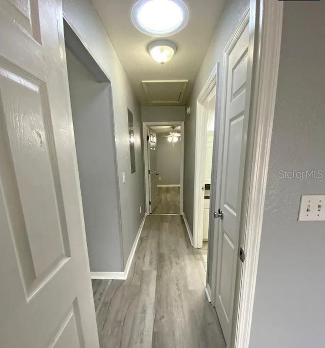 hallway with attic access, baseboards, and light wood finished floors