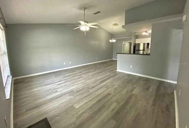 unfurnished living room with visible vents, ceiling fan with notable chandelier, baseboards, dark wood-style flooring, and vaulted ceiling