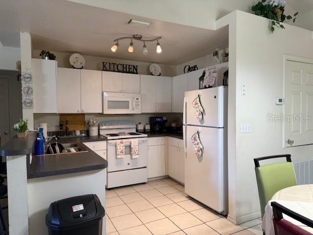 kitchen featuring dark countertops, visible vents, light tile patterned flooring, white appliances, and a sink