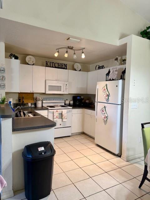 kitchen with a sink, white appliances, dark countertops, and white cabinetry