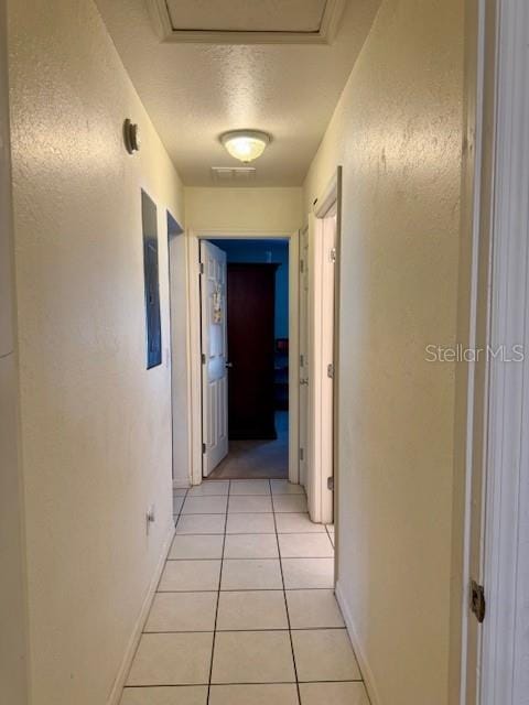 corridor featuring baseboards, attic access, a textured wall, light tile patterned flooring, and a textured ceiling