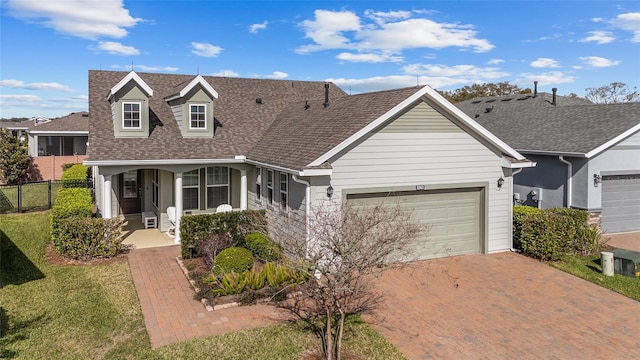 view of front of home with decorative driveway, roof with shingles, covered porch, an attached garage, and fence