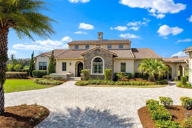 mediterranean / spanish-style home featuring stone siding, a front yard, a tiled roof, and stucco siding