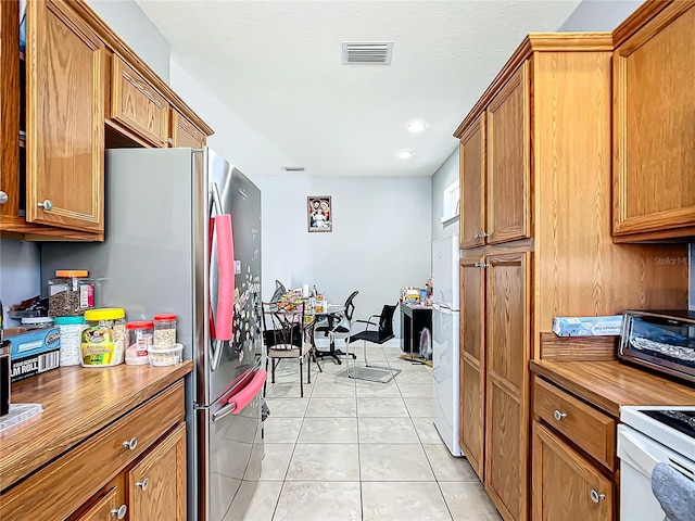 kitchen with a toaster, light tile patterned floors, visible vents, brown cabinetry, and butcher block countertops