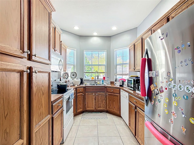 kitchen with brown cabinets, light tile patterned floors, recessed lighting, a sink, and white appliances