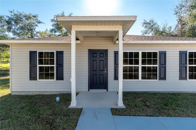 doorway to property featuring a lawn and a shingled roof