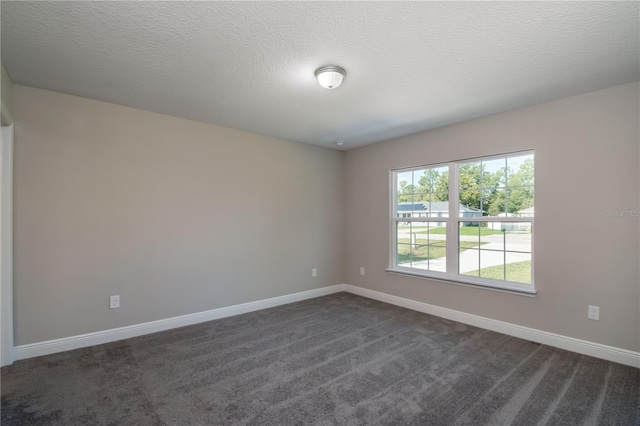 empty room with a textured ceiling, dark carpet, and baseboards