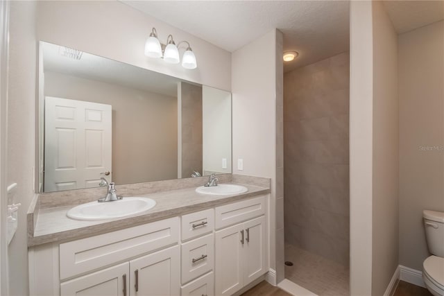 full bathroom featuring a sink, a tile shower, toilet, and double vanity