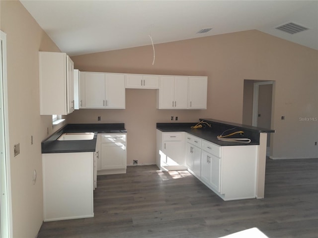 kitchen featuring vaulted ceiling, dark wood finished floors, dark countertops, white cabinetry, and a sink