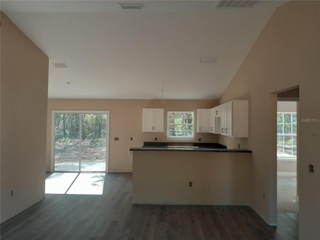 kitchen featuring wood finished floors, white cabinetry, dark countertops, a peninsula, and vaulted ceiling