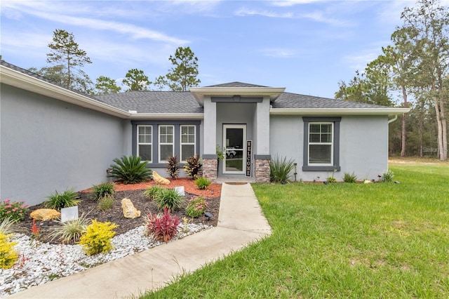 view of front facade with stucco siding, stone siding, roof with shingles, and a front yard