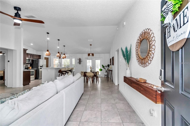 living area featuring light tile patterned floors, a textured ceiling, a ceiling fan, and vaulted ceiling