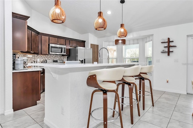 kitchen with light tile patterned flooring, stainless steel appliances, light countertops, vaulted ceiling, and dark brown cabinetry