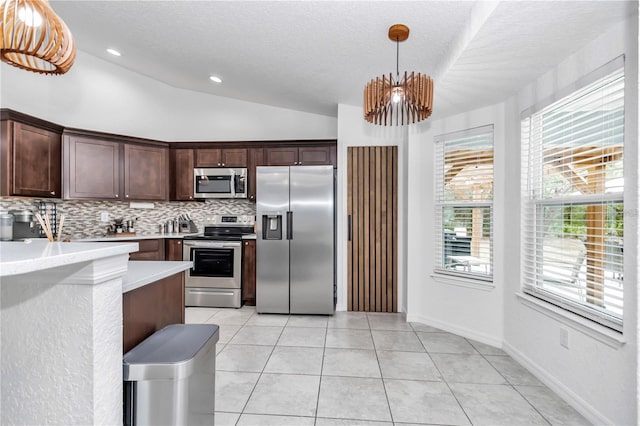 kitchen featuring light tile patterned floors, stainless steel appliances, vaulted ceiling, light countertops, and dark brown cabinets