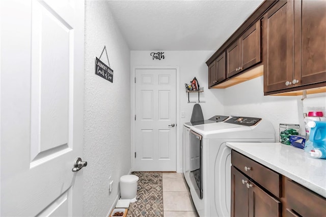 clothes washing area featuring washer and dryer, a textured ceiling, cabinet space, light tile patterned floors, and a textured wall