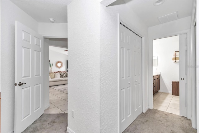 corridor with light tile patterned flooring, light colored carpet, and visible vents