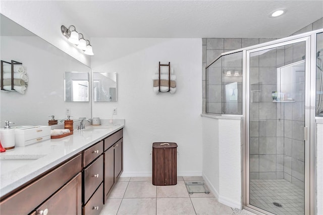 bathroom with tile patterned flooring, baseboards, double vanity, a stall shower, and a sink