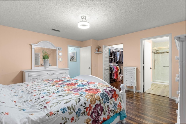 bedroom with a textured ceiling, wood finished floors, visible vents, baseboards, and a closet