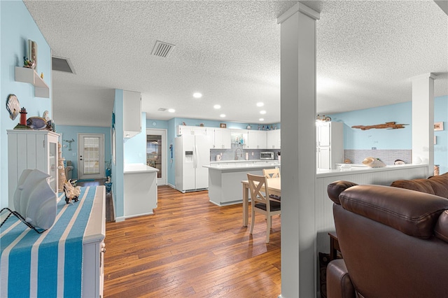 interior space featuring white refrigerator with ice dispenser, visible vents, white cabinets, open floor plan, and light wood finished floors