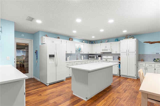 kitchen featuring dark wood finished floors, visible vents, a kitchen island, a sink, and white appliances