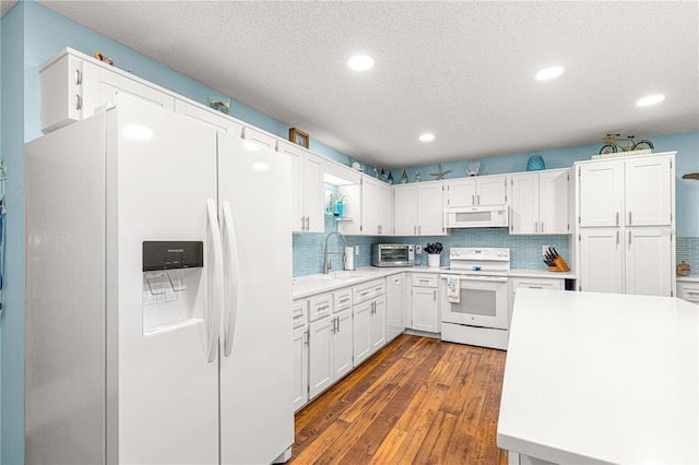 kitchen featuring white appliances, a sink, white cabinets, light countertops, and dark wood-style floors