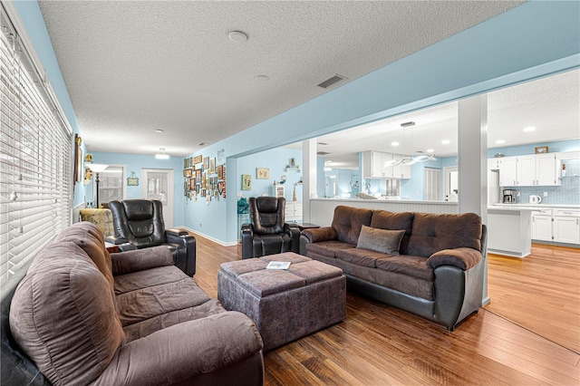 living room with light wood-type flooring, visible vents, and a textured ceiling