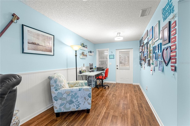 office area with a wainscoted wall, a textured ceiling, wood finished floors, and visible vents