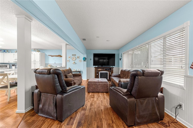 living room featuring decorative columns, a fireplace, visible vents, a textured ceiling, and wood finished floors