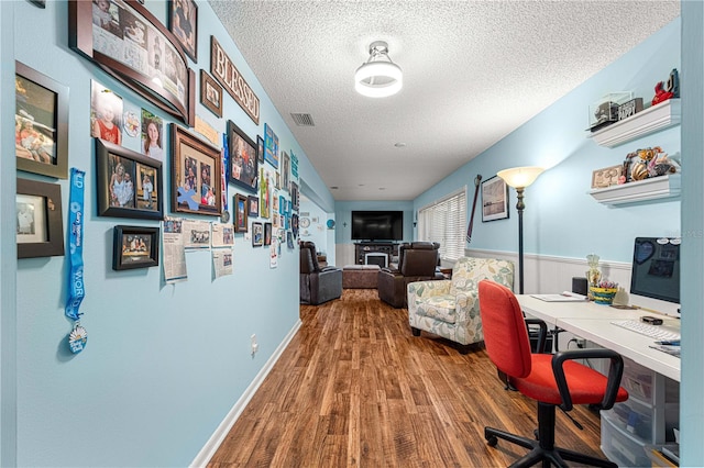 home office featuring a wainscoted wall, visible vents, a textured ceiling, and wood finished floors