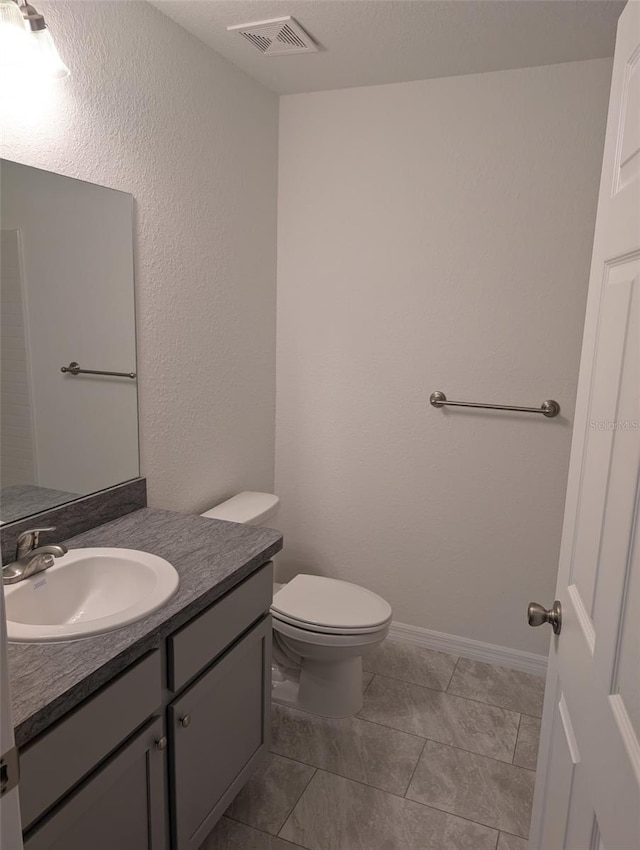 bathroom with toilet, vanity, visible vents, and baseboards