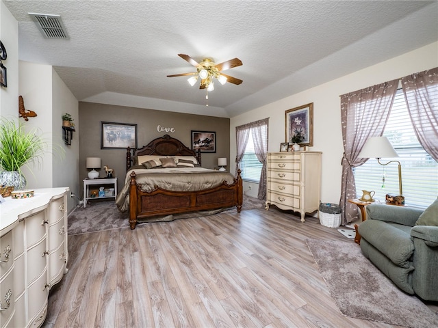 bedroom with light wood-type flooring, ceiling fan, visible vents, and a textured ceiling